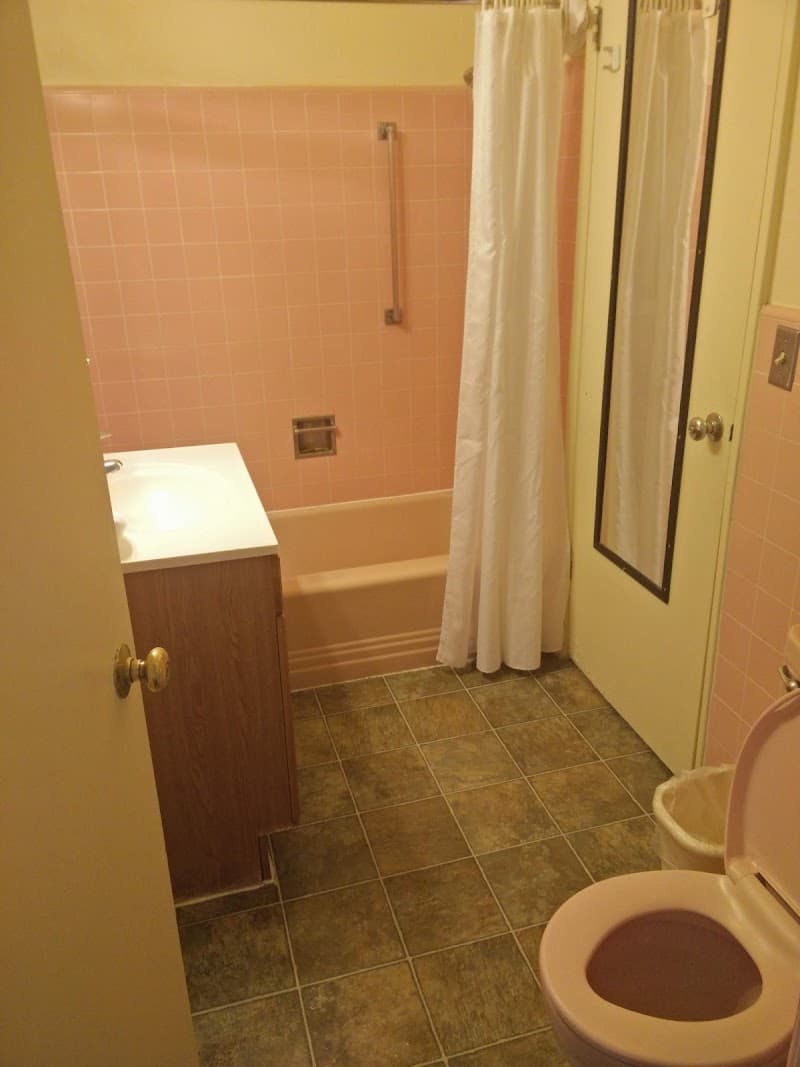 A cozy motel bathroom with pink tiled walls, a bathtub, sink, toilet, and a white shower curtain creates a retro vibe ideal for travelers seeking vintage charm at the Crown Motel in Kings Beach, California.