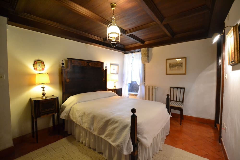 A cozy bedroom with rustic wooden beams, warm lighting from bedside lamps, and terracotta flooring evokes a serene and inviting atmosphere, perfect for travelers seeking a charming and traditional accommodation experience.