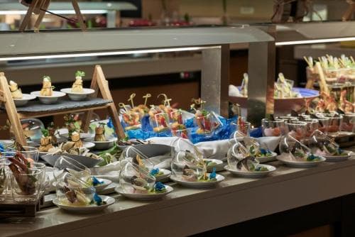 A vibrant buffet spread featuring an array of colorful appetizers and desserts on a sleek counter, ideal for travelers seeking a luxurious dining experience in a modern hotel setting.