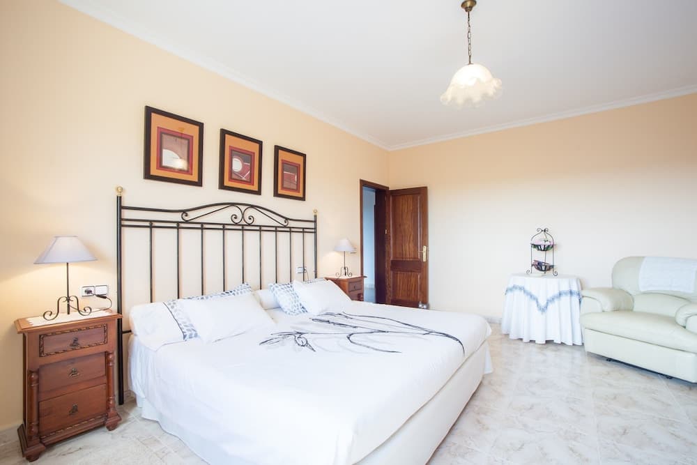 A cozy bedroom with a white bed, wooden nightstands, framed wall art, and a leather armchair creates a serene atmosphere ideal for vacation rentals or hotel stays.