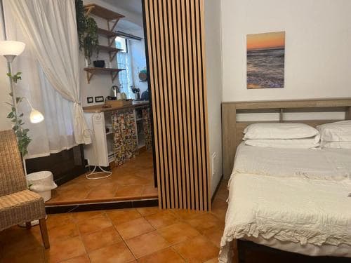 A cozy studio apartment with terracotta flooring, a neatly made bed, a wooden divider, and a small kitchenette, exudes a warm and inviting atmosphere perfect for a relaxing solo getaway.