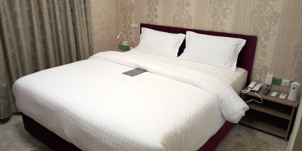 A cozy hotel room features a neatly made bed with white linens against patterned wallpaper, accompanied by bedside tables with modern amenities, ideal for travelers seeking comfort and convenience.