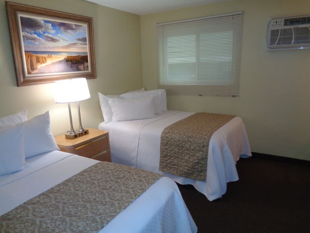 A cozy hotel room features two neatly made beds with white linens, a beach-themed artwork, and soft lighting, ideal for travelers seeking comfort and relaxation.