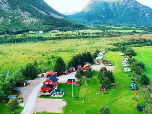 A serene camping site nestled in a lush green valley surrounded by majestic mountains, featuring colorful cabins and tents, ideal for nature lovers seeking a peaceful retreat.