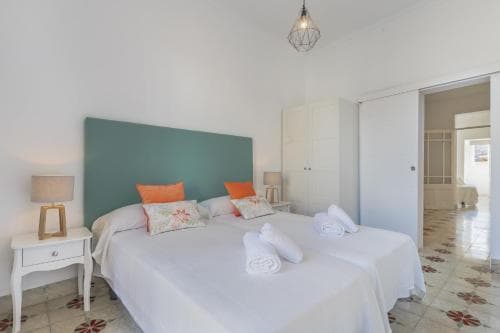 A cozy bedroom with a teal headboard, white furnishings, and patterned tiles exudes a serene and inviting atmosphere, perfect for travelers seeking relaxation in a charming accommodation setting.