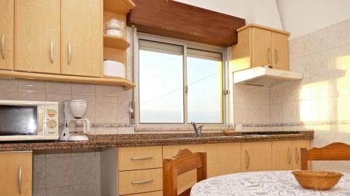 A cozy kitchen with wooden cabinets, a tiled backsplash, and a dining table bathed in natural light through a large window, ideal for travelers seeking a homey and functional rental space.