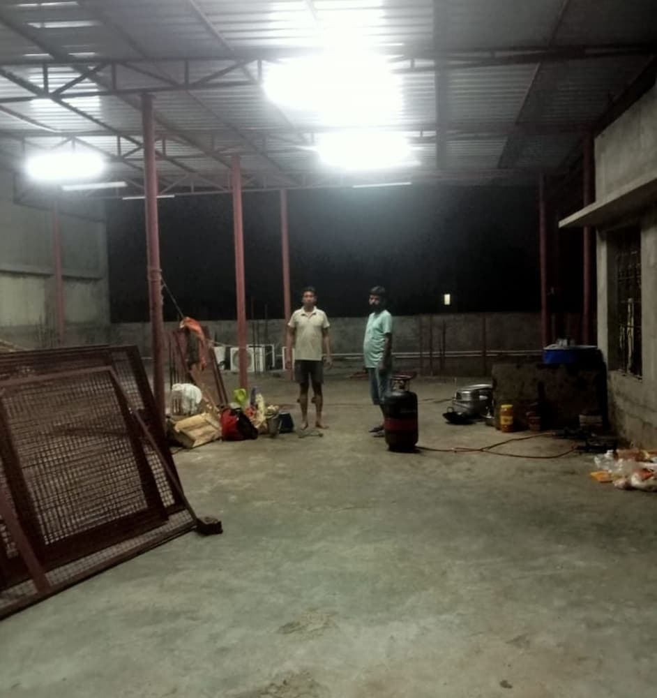 A dimly lit industrial warehouse with two individuals amidst scattered tools and equipment creates an atmosphere of quiet productivity, ideal for travelers seeking authentic local work environments.