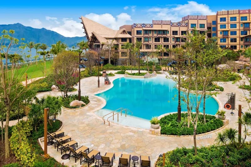 A vibrant tropical resort scene featuring a serene pool surrounded by lush greenery and modern buildings under a bright blue sky, ideal for family vacations seeking relaxation and adventure in a picturesque setting.