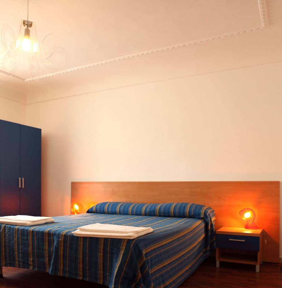 A cozy hotel room features a neatly made bed with blue striped bedding, warm ambient lighting from bedside lamps, and a minimalist decor ideal for travelers seeking comfort and simplicity.