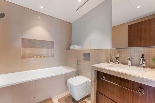 A modern bathroom with sleek white fixtures, wooden cabinetry, and ambient lighting creates a serene atmosphere ideal for relaxation during a luxury hotel stay.