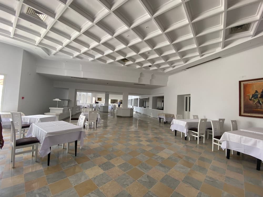 A spacious, elegant dining hall with a checkered floor, white tables and chairs, and a geometric ceiling creates an inviting atmosphere ideal for travelers seeking a refined dining experience.
