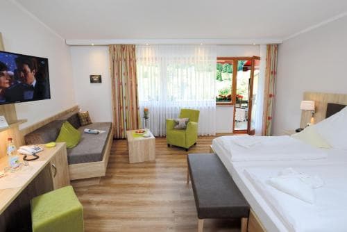 A cozy hotel room with a neatly made bed, vibrant green accents, and a balcony view of lush greenery, ideal for travelers seeking comfort and relaxation in a serene setting.
