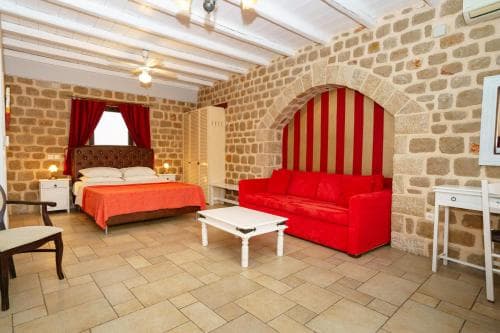 A cozy rustic bedroom with stone walls, wooden beams, and vibrant red accents creates an inviting atmosphere, perfect for travelers seeking a charming and intimate retreat.