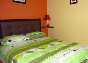 A cozy hotel room features a vibrant green bedspread against warm orange walls, creating an inviting atmosphere perfect for travelers seeking comfort and relaxation.