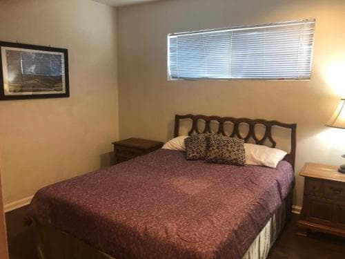A cozy bedroom with a neatly made bed adorned in burgundy bedding, wooden furniture, and soft lighting creates a serene atmosphere ideal for travelers seeking a comfortable stay.