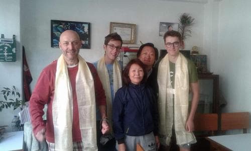 A group of travelers wearing traditional scarves stands together in a cozy indoor setting adorned with cultural decorations, evoking a warm and welcoming atmosphere ideal for cultural exchange experiences.