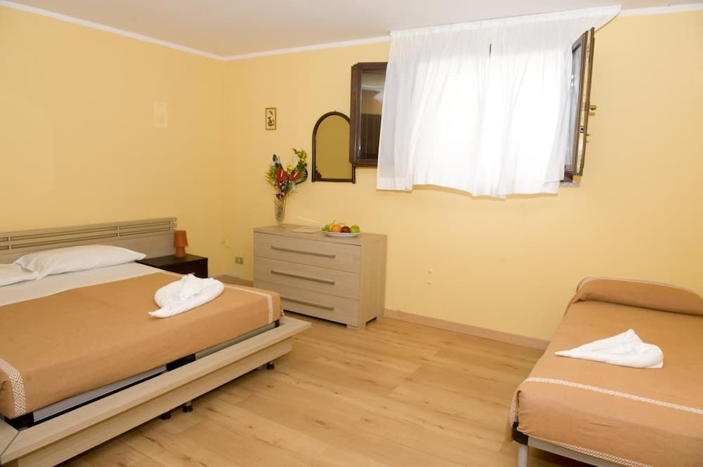 A cozy hotel room with two neatly made beds, warm yellow walls, wooden flooring, and a window with white curtains offers a comfortable stay for travelers seeking simplicity and relaxation.