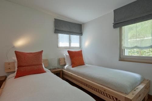 A cozy twin-bedroom with wooden beds, orange pillows, and natural light filtering through windows, ideal for a serene retreat or family vacation accommodation.