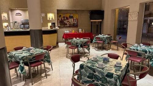 A cozy indoor café with patterned tablecloths, red chairs, and warm lighting creates an inviting atmosphere, perfect for travelers seeking a relaxing dining spot.