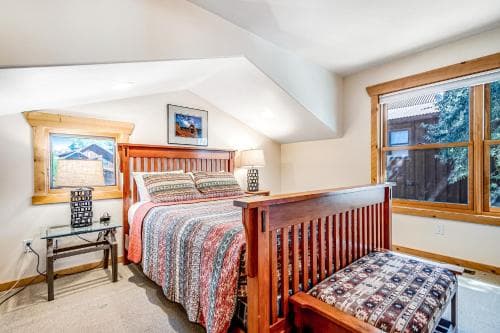A cozy attic bedroom with a wooden bed, vibrant patterned bedding, and large windows offering a serene view of trees, ideal for a relaxing getaway retreat.