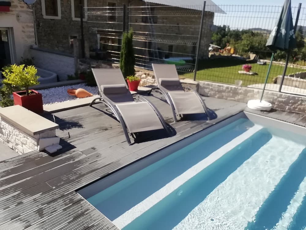 A serene private poolside retreat features sun loungers on a wooden deck, surrounded by lush greenery and stone architecture, ideal for relaxing vacations.