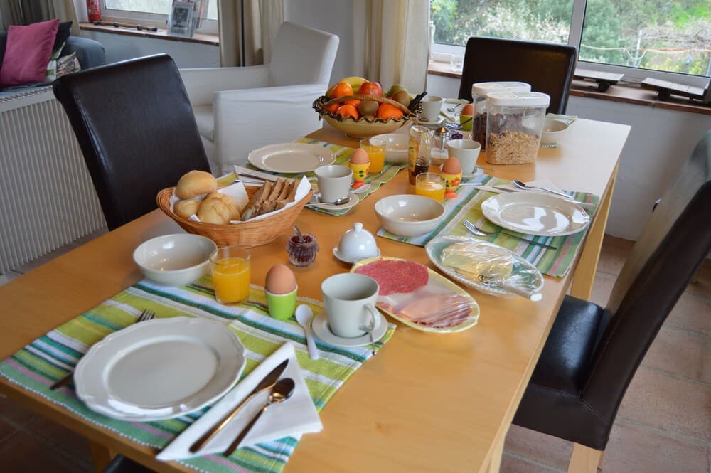 A cozy dining room set for breakfast with fresh bread, eggs, juice, and fruit, inviting travelers to enjoy a warm morning meal in a comfortable home-like setting.