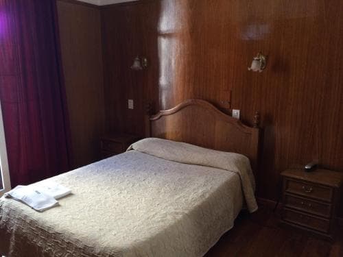 A cozy hotel room with warm wooden paneling, a neatly made bed, bedside tables, and soft lighting creates an inviting atmosphere ideal for travelers seeking comfort and relaxation.