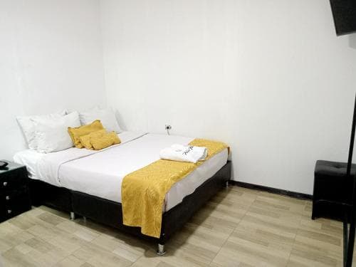 A cozy hotel room features a neatly made bed with yellow accents, minimalist decor, and wooden flooring, ideal for travelers seeking comfort and simplicity.