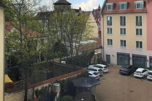 A serene urban courtyard framed by historic buildings, lush greenery, and parked cars offers a tranquil retreat ideal for city explorers seeking a peaceful hideaway.