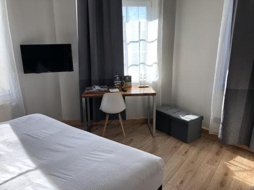 A cozy hotel room with a neatly made bed, wooden desk by the window, and modern amenities creates a serene atmosphere ideal for travelers seeking comfort and convenience.