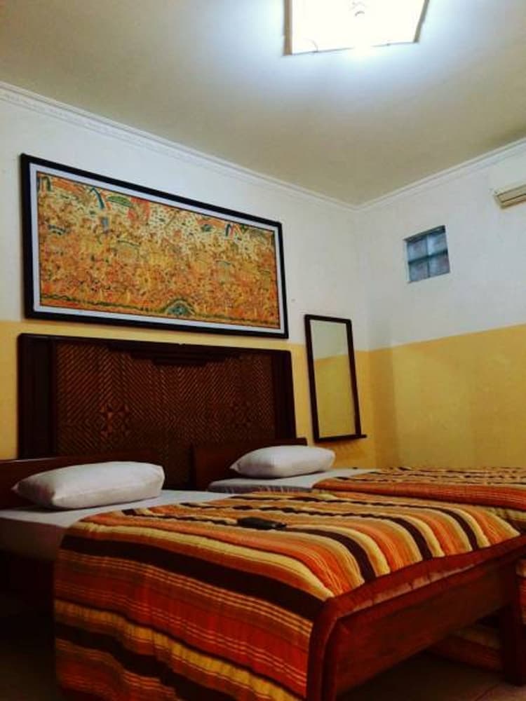 A cozy hotel room features two beds adorned with vibrant striped blankets, a decorative headboard, and a colorful wall art piece, creating a warm and inviting atmosphere ideal for travelers seeking comfort.