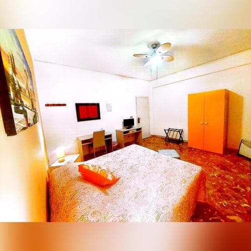 A cozy apartment bedroom with a patterned bedspread, vibrant orange wardrobe, and eclectic decor offers a warm and inviting atmosphere for travelers seeking a comfortable stay.