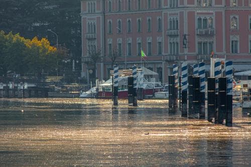 A serene waterfront scene with historic buildings reflecting on calm waters, lined by mooring posts and boats, evokes a tranquil European charm ideal for leisurely city breaks.