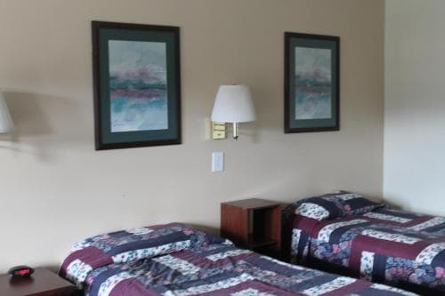 A cozy hotel room features two neatly made beds with patterned quilts, framed abstract art on the walls, and a bedside lamp, ideal for travelers seeking comfort and simplicity.