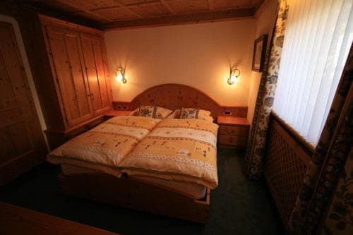 A cozy, rustic bedroom with wooden furnishings, warm lighting, and floral curtains creates an inviting atmosphere ideal for travelers seeking a comfortable retreat in a traditional lodge setting.