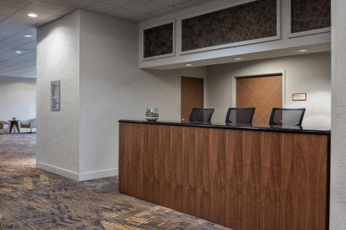 A modern hotel lobby features a sleek wooden reception desk with black chairs, set against neutral walls and patterned carpeting, creating a welcoming atmosphere ideal for travelers seeking professional service.