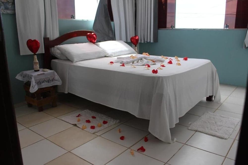 A cozy hotel room with a neatly arranged bed adorned with rose petals, heart-shaped decorations, and soft lighting creates a romantic atmosphere ideal for a couples' getaway.