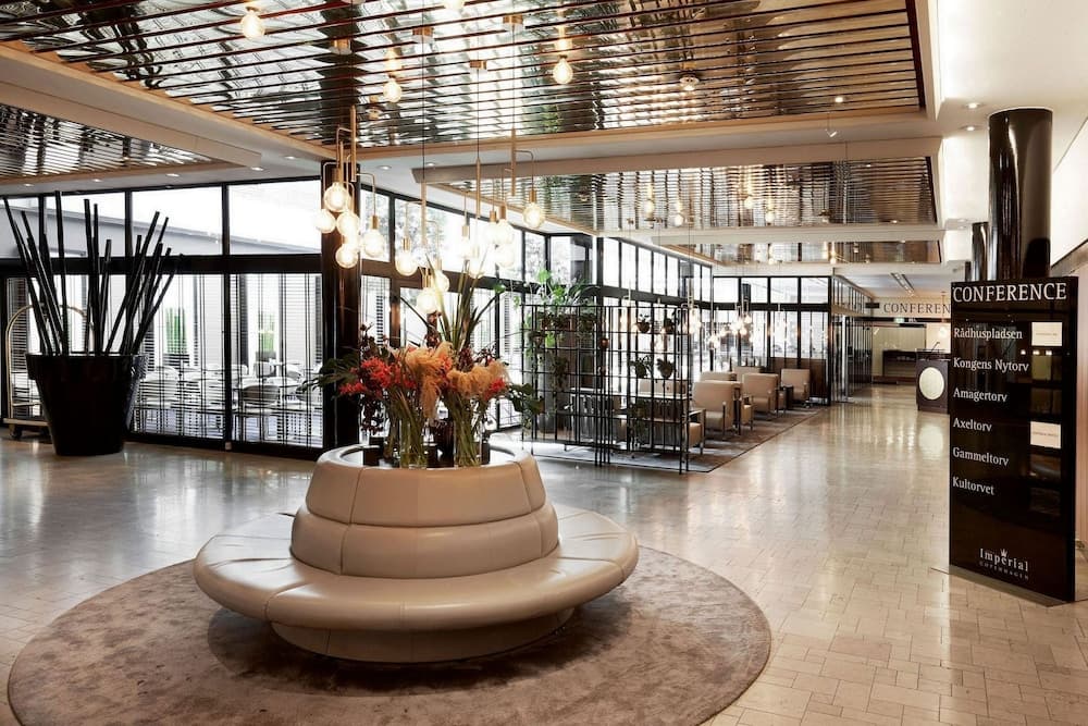 A modern hotel lobby features sleek seating, vibrant floral arrangements, and a glass-paneled ceiling, creating an inviting atmosphere ideal for business travelers seeking conference facilities.