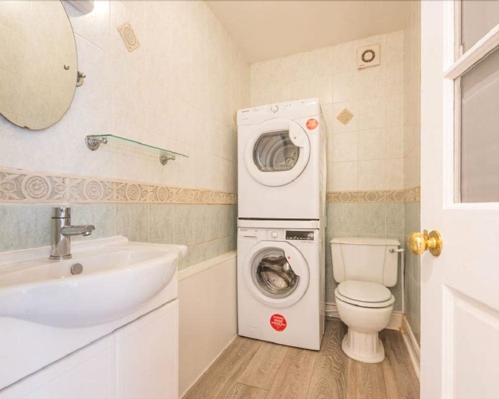 A cozy bathroom with a stacked washer-dryer unit, white sink vanity, toilet, and decorative tiled walls offers a practical and inviting space for travelers seeking convenience in their accommodations.