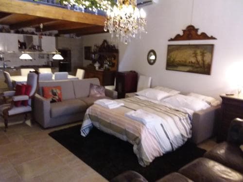 A cozy, rustic apartment features a bedroom with a neatly made bed, a plush sofa, and a chandelier, creating an inviting atmosphere ideal for travelers seeking comfort in a charming, homey setting.