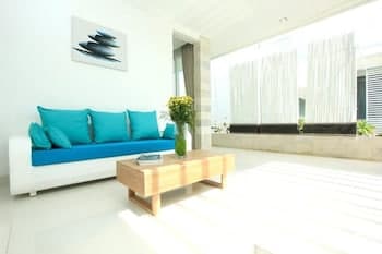 A serene modern living room with turquoise cushions, wooden coffee table, and large windows draped in sheer curtains, ideal for a tranquil vacation rental experience.