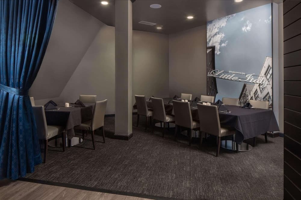 A cozy private dining room with elegant blue curtains, modern tables set for a meal, and a mural of "Little Italy," ideal for intimate gatherings or business meetings.