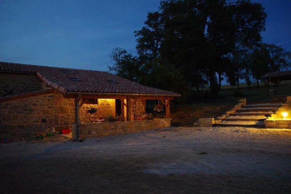 A serene evening at a rustic stone cottage with warm outdoor lighting, surrounded by trees, ideal for a tranquil countryside getaway.