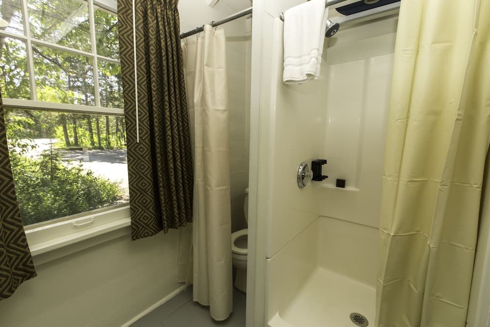 A cozy bathroom with a shower, toilet, and window offering a serene forest view, ideal for travelers seeking relaxation in a tranquil setting.