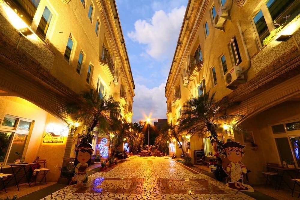 A charming evening street scene illuminated by warm lights, featuring decorative statues, palm trees, and cozy outdoor seating, evokes a relaxed and inviting atmosphere perfect for travelers seeking a unique cultural experience.