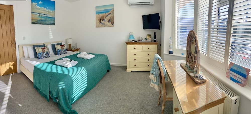 A cozy beach-themed bedroom with a neatly made bed, ocean artwork, and a sunny window view invites travelers seeking a relaxing seaside retreat.
