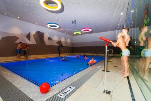Children enjoy playful moments in an indoor pool illuminated by colorful ceiling lights, surrounded by mountain-themed decor, ideal for family-friendly resort stays.