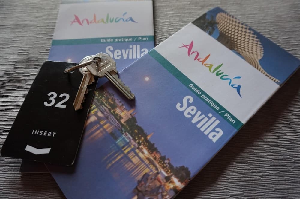 A serene travel setup featuring "Andalucía Sevilla" guidebooks and keys on a textured surface, ideal for planning a cultural getaway in Spain's vibrant city.