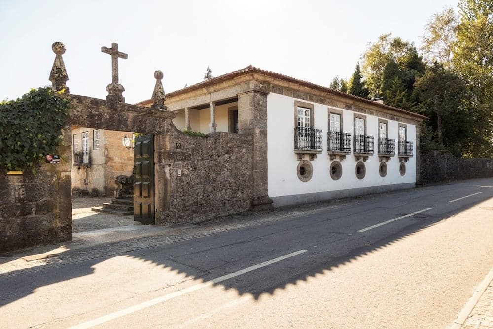 A serene rural scene features a historic stone building with ornate balconies and a cross-topped gate, ideal for cultural heritage tourism and exploring quaint countryside architecture.