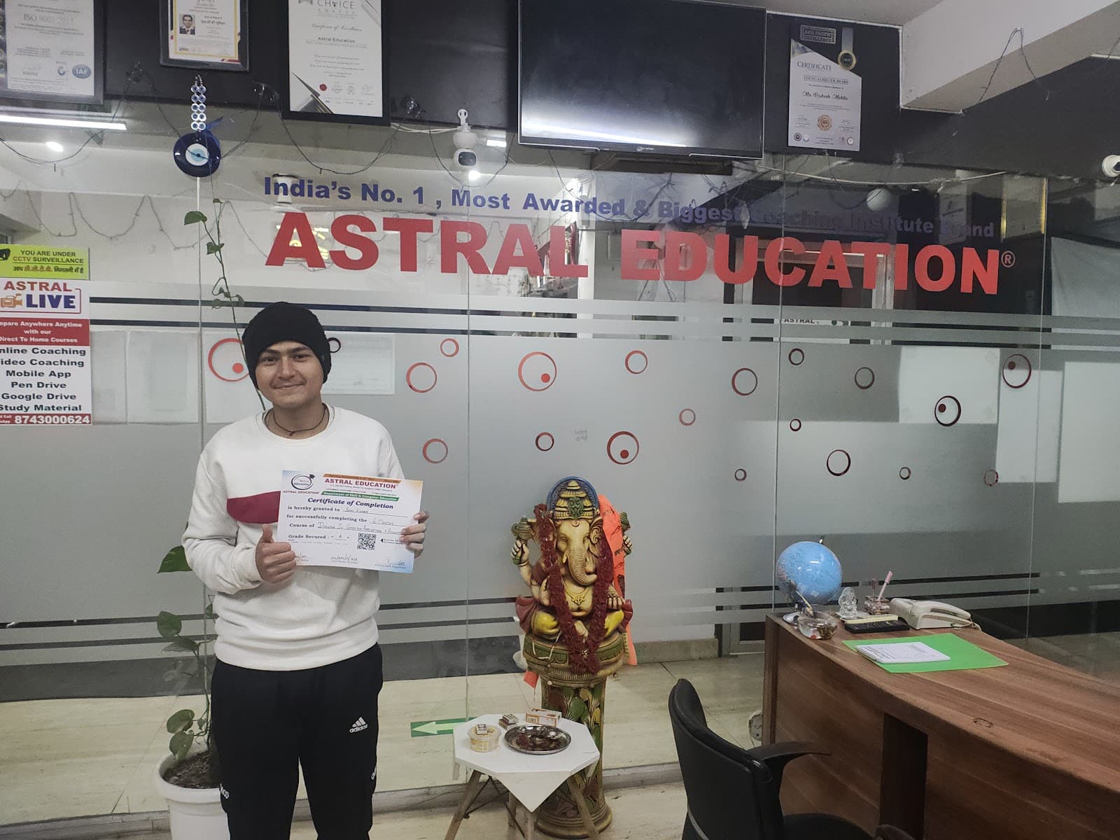 A proud student displays his certificate in the vibrant office of Astral Education, featuring a Ganesha statue and certificates on display, ideal for educational travelers seeking top coaching institutes in Gurugram, India.